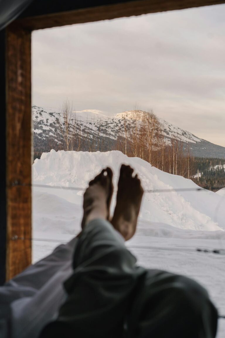 Peaceful winter morning with feet propped up, overlooking snowy mountains through a window.